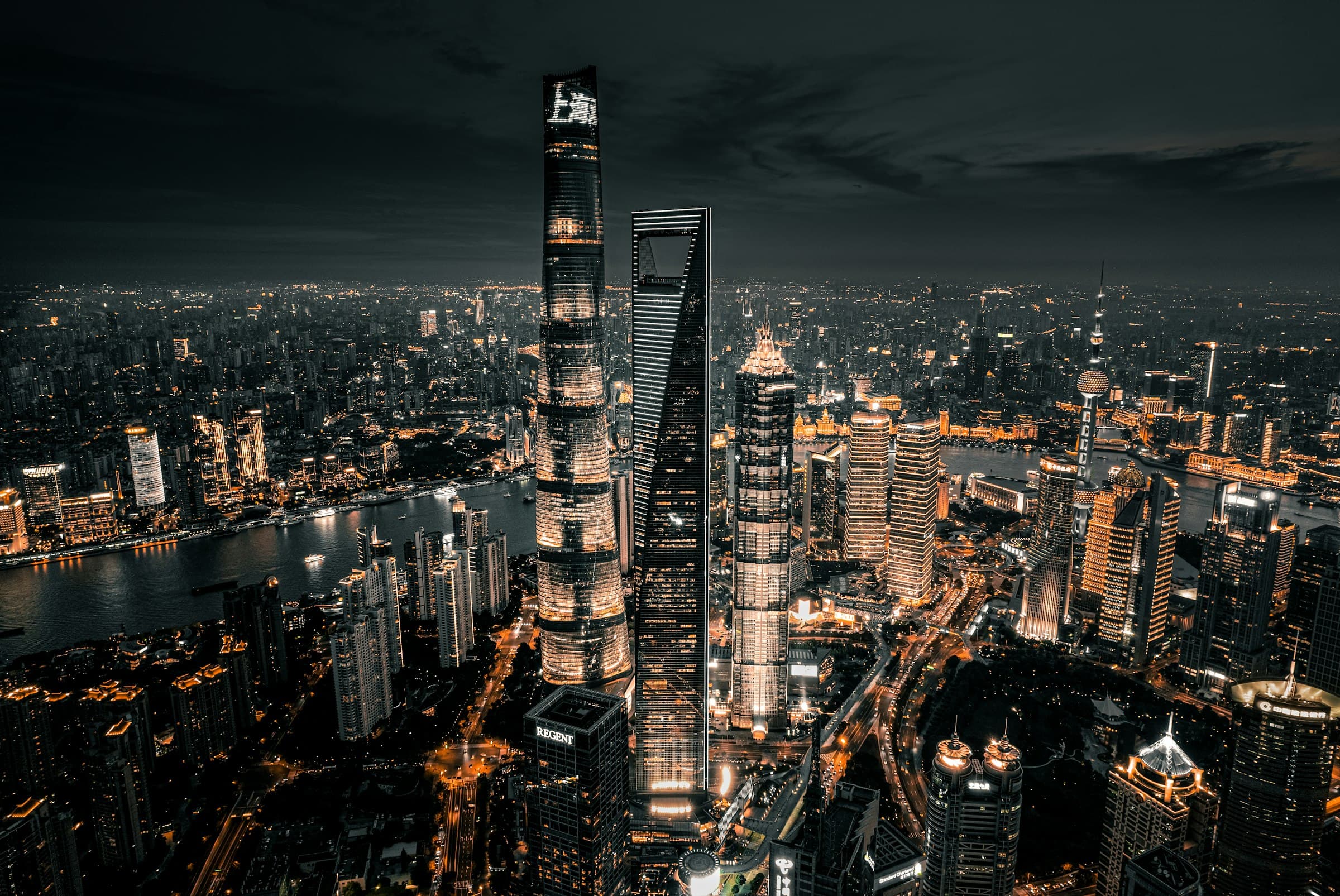 The lit towers of Lujiazui at night, seen from above, with the Huangpu River curving behind them